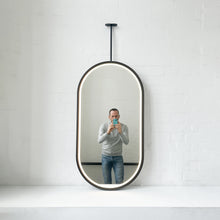 Modern front illuminated Capsula™ ceiling suspended pill shaped mirror with a black powder coated full frame.