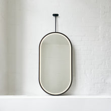 Modern front illuminated Capsula™ ceiling suspended pill shaped mirror with a black powder coated full frame