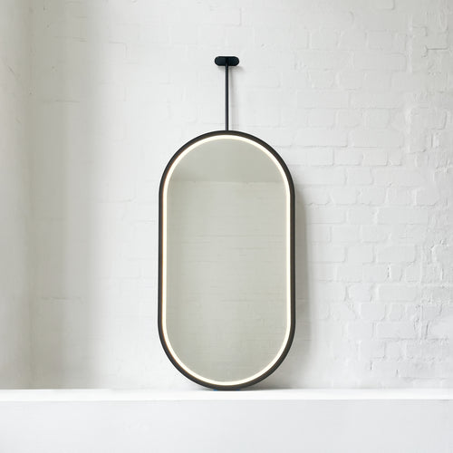 Modern front illuminated Capsula™ ceiling suspended pill shaped mirror with a black powder coated full frame