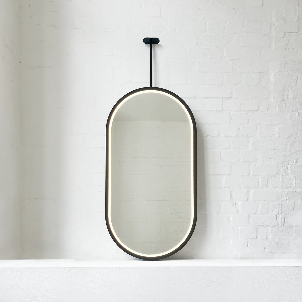 Modern front illuminated Capsula™ ceiling suspended pill shaped mirror with a black powder coated full frame