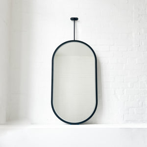 Modern front illuminated Capsula™ ceiling suspended pill shaped mirror with a black powder coated full frame